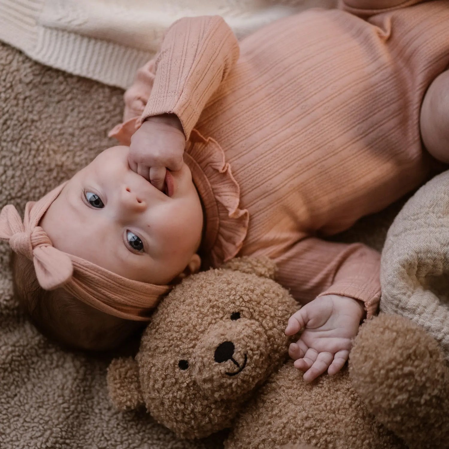 Baby in roséfarbener Kleidung der Marke Dirkje, liegend mit einem Plüschbären, präsentiert im Mokkini Kindermode Online-Shop